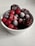 A white bowl filled with an assortment of frozen berries, including blackberries, raspberries, and cherries. A light layer of frost coats the berries, highlighting their texture and rich colors.