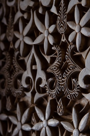 Intricate floral and geometric patterns are carved into a wooden surface. The design features overlapping flowers and swirling shapes, with detailed engraving work that adds depth and texture.