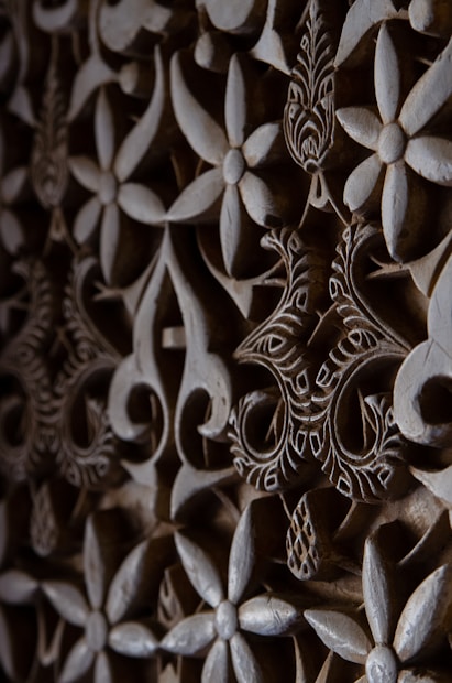 Intricate floral and geometric patterns are carved into a wooden surface. The design features overlapping flowers and swirling shapes, with detailed engraving work that adds depth and texture.
