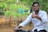 A smiling young Indian man giving a thumbs up outdoors.