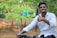 A smiling young Indian man giving a thumbs up outdoors.