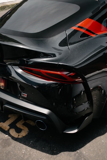 A sleek black sports car featuring a glossy finish and red accents. The rear section of the vehicle is highlighted, displaying the taillights and distinctive design elements.