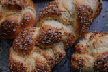 Freshly baked braided loaves of bread topped with a generous sprinkling of sesame and poppy seeds, resting on a dark baking tray.