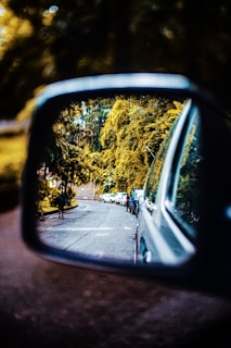 Close-up of a white taxi’s side mirror reflecting the vibrant greenery of Assam’s tea estates.