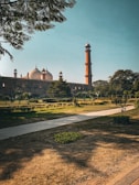 A historic mosque with large domes and a tall minaret stands elegantly against a clear blue sky. It is surrounded by well-maintained gardens and pathways. The lush greenery and precise architectural features highlight the grandeur of the structure.