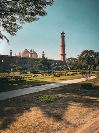 A historic mosque with large domes and a tall minaret stands elegantly against a clear blue sky. It is surrounded by well-maintained gardens and pathways. The lush greenery and precise architectural features highlight the grandeur of the structure.