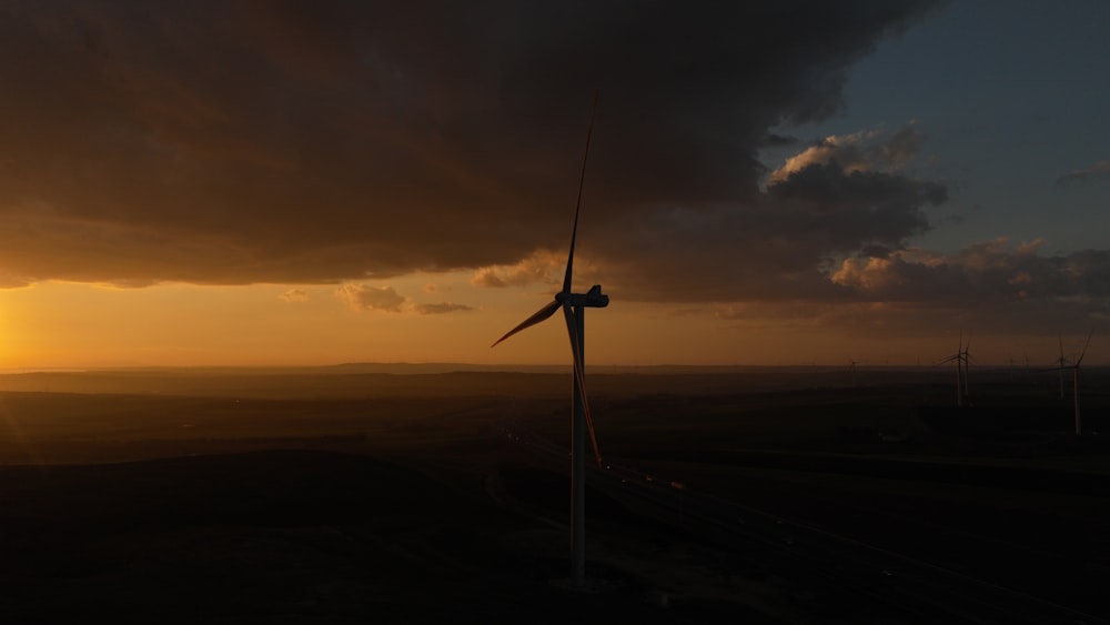the sun is setting behind a wind turbine
