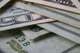 A close-up view of multiple U.S. dollar bills arranged in an overlapping manner. The intricate details of the currency's security features and patterns are visible, showing shades of green and grey.