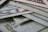 A close-up view of multiple U.S. dollar bills arranged in an overlapping manner. The intricate details of the currency's security features and patterns are visible, showing shades of green and grey.