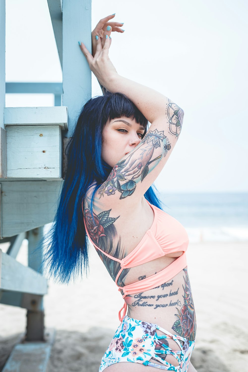 a woman with blue hair and tattoos posing on the beach