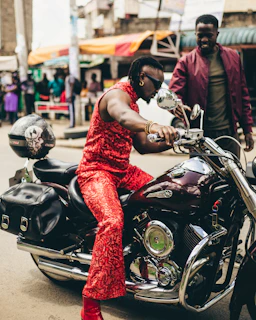 A shiny red motorbike parked near a bustling local market with colorful stalls