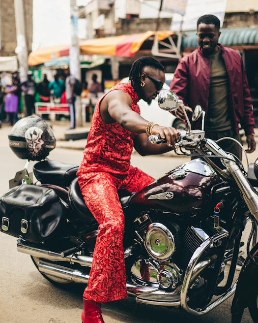 A shiny red motorbike parked near a bustling local market with colorful stalls