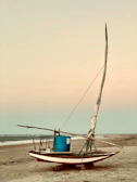 A traditional island fishing boat resting on a sandy beach at sunset.