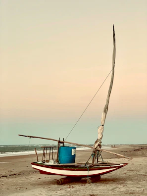 A traditional island fishing boat resting on a sandy beach at sunset.