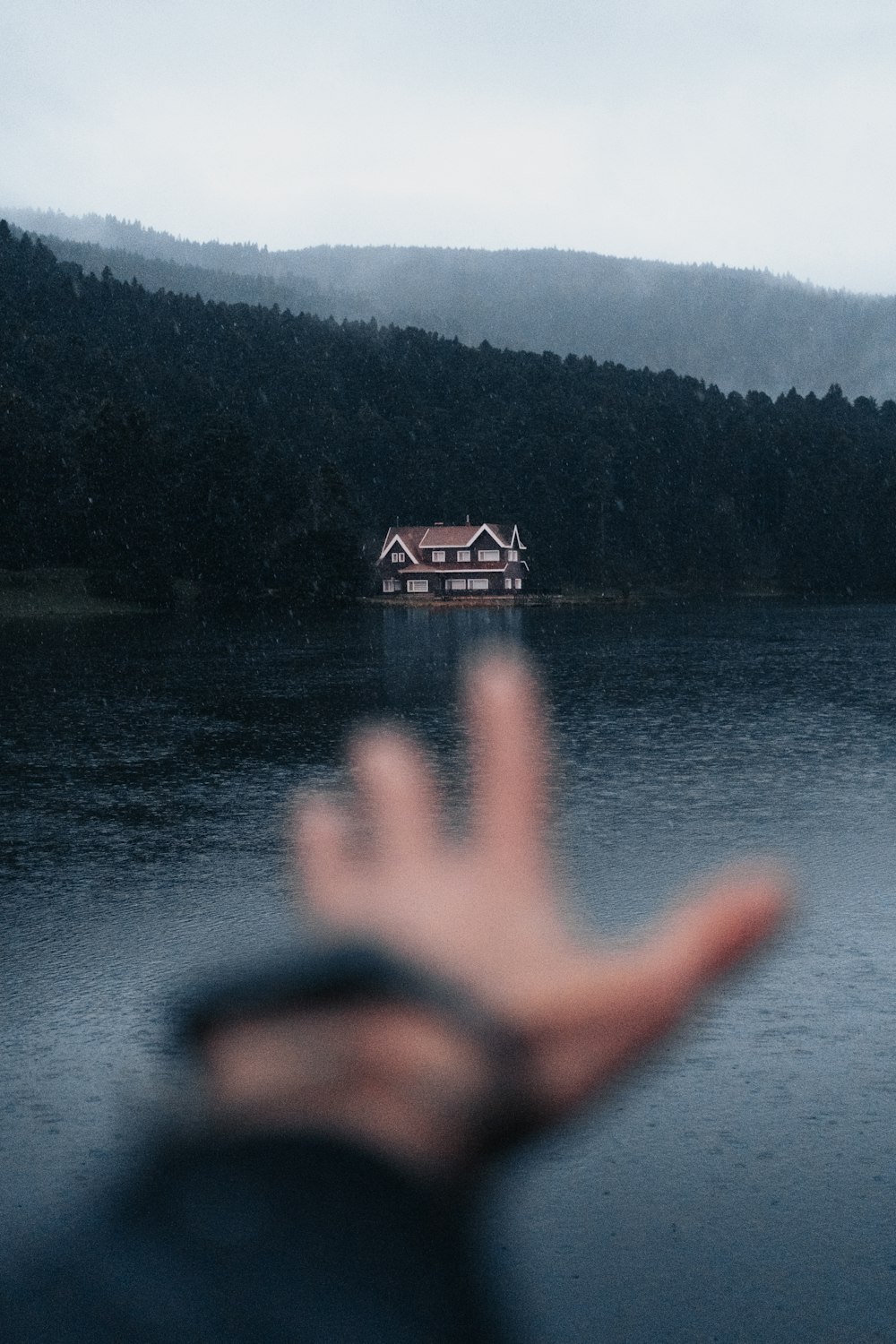 a hand is in front of a house on a lake