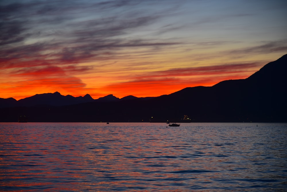 a boat in the water at sunset with mountains in the background