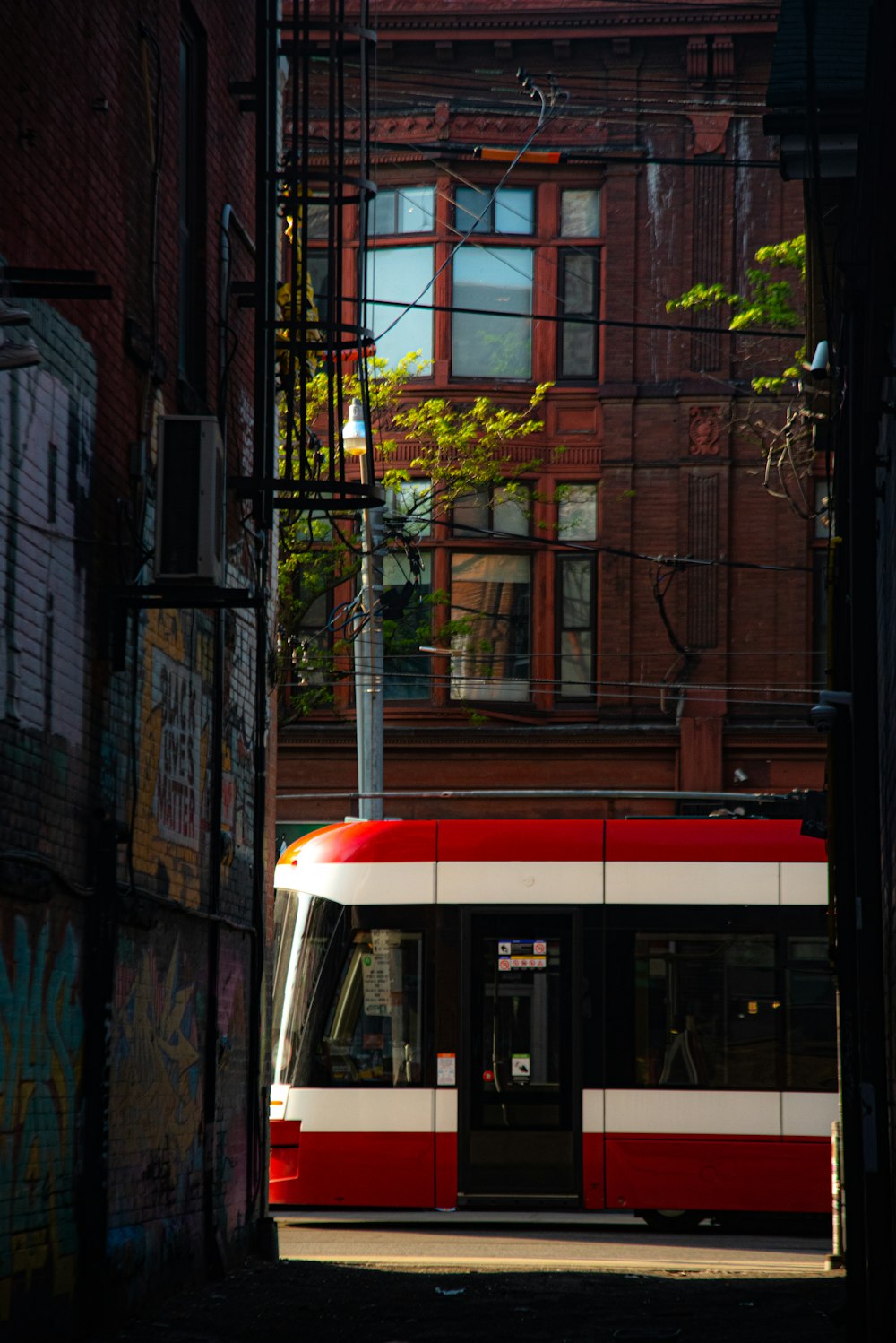 a red and white train traveling down a street next to a tall building