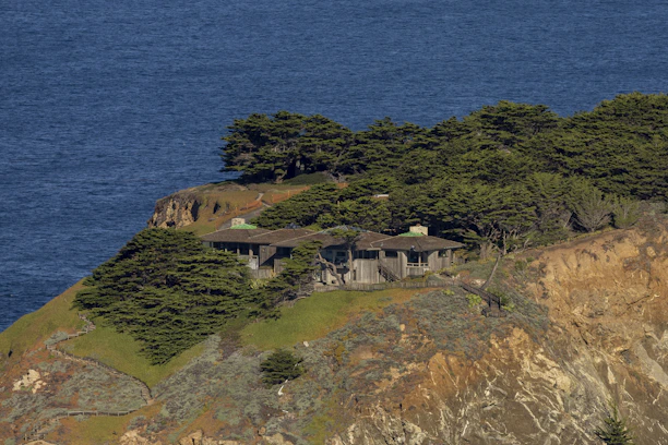 A sleek modern coastal house with glass facades and a green living roof nestled against the rugged Scottish coastline.