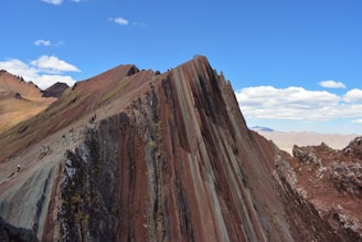 Colorful layers of Rainbow Mountain under a bright blue sky with hikers admiring the view.