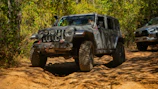 A rugged SUV driving through a forest trail with dust kicking up.