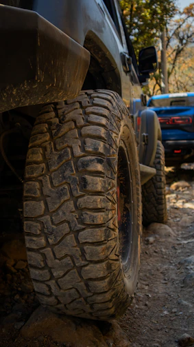 Close-up of rugged off-road tires gripping rocky terrain, dust swirling around.