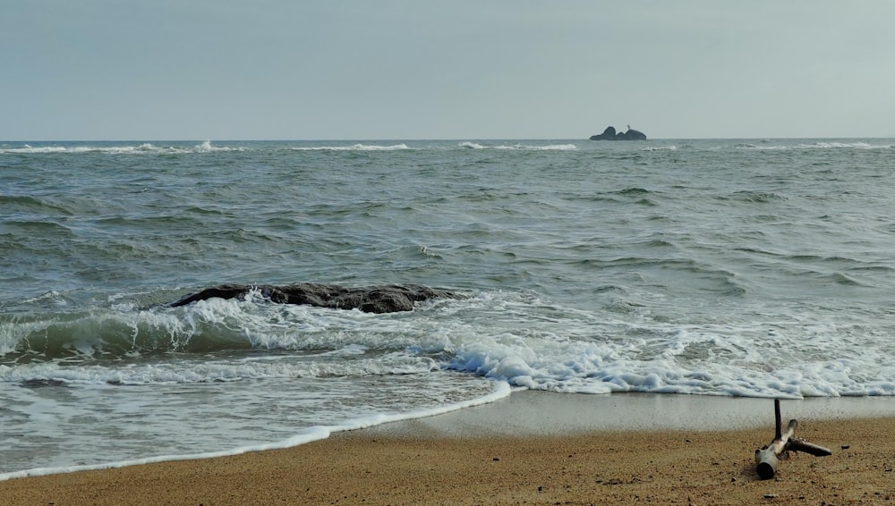 a beach with waves coming in to shore and a small island in the distance