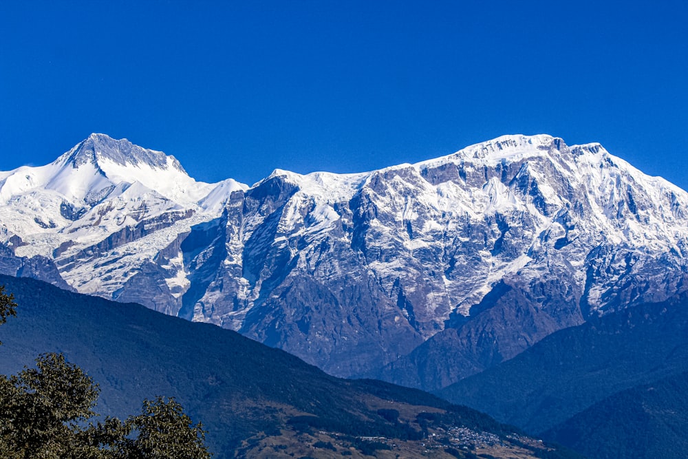 a snow covered mountain range with trees in the foreground