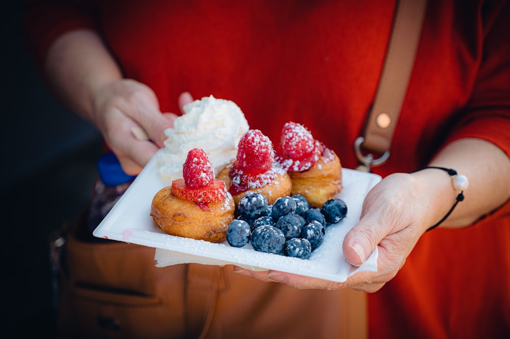 a person holding a plate of pastries and berries