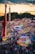 A vibrant amusement park bustling with people enjoying various rides and attractions under a twilight sky. Brightly lit signs advertise games and food stalls, including funnel cakes and corn dogs. Roller coasters and thrill rides are prominent, with colorful lights illuminating the scene.