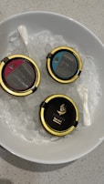 A white bowl filled with ice holds three tins of caviar with gold lids, labeled as Caspiran brand. Two small, white spoons are also placed in the bowl.