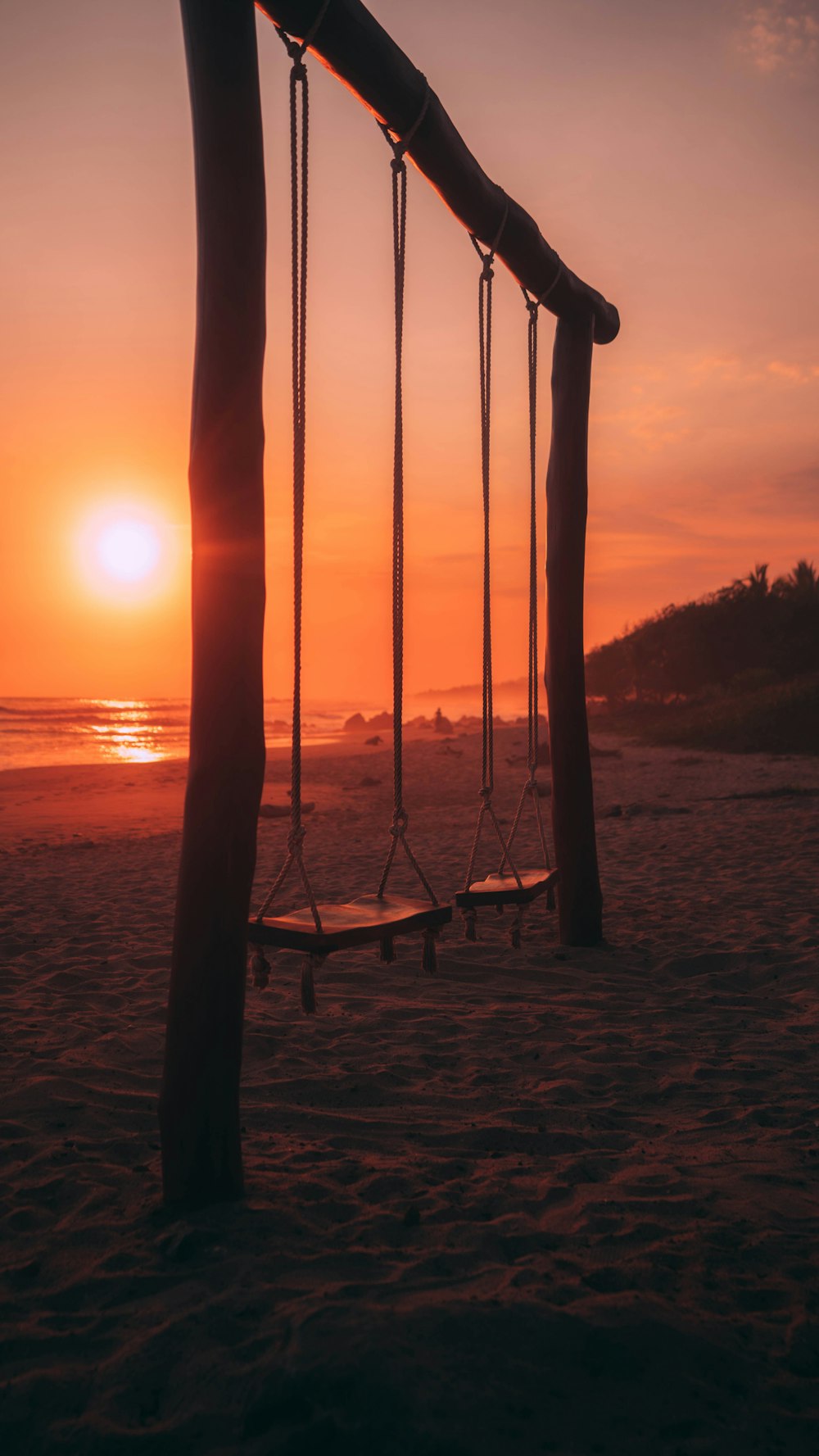 the sun is setting behind a row of swings on the beach