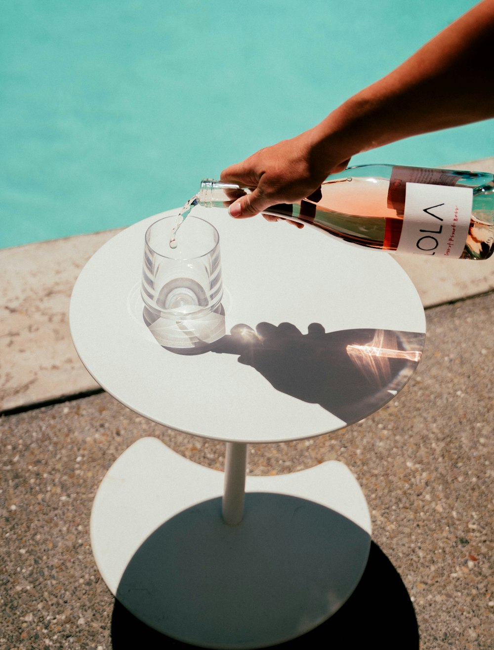 a person pouring a glass of wine on a table next to a pool