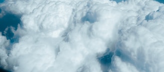A vast expanse of fluffy, white clouds with varying textures. The clouds appear soft and voluminous, floating against a backdrop of blue sky.