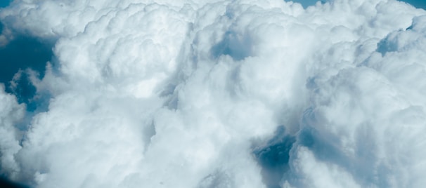 A vast expanse of fluffy, white clouds with varying textures. The clouds appear soft and voluminous, floating against a backdrop of blue sky.