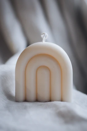 A minimalist candle with a smooth cream surface casting a warm glow in a serene room.