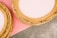 Ornate golden picture frames with intricate floral designs are placed partially on a pink surface and a gray textured background. The frames have an empty center, indicating they are not currently holding any artwork.