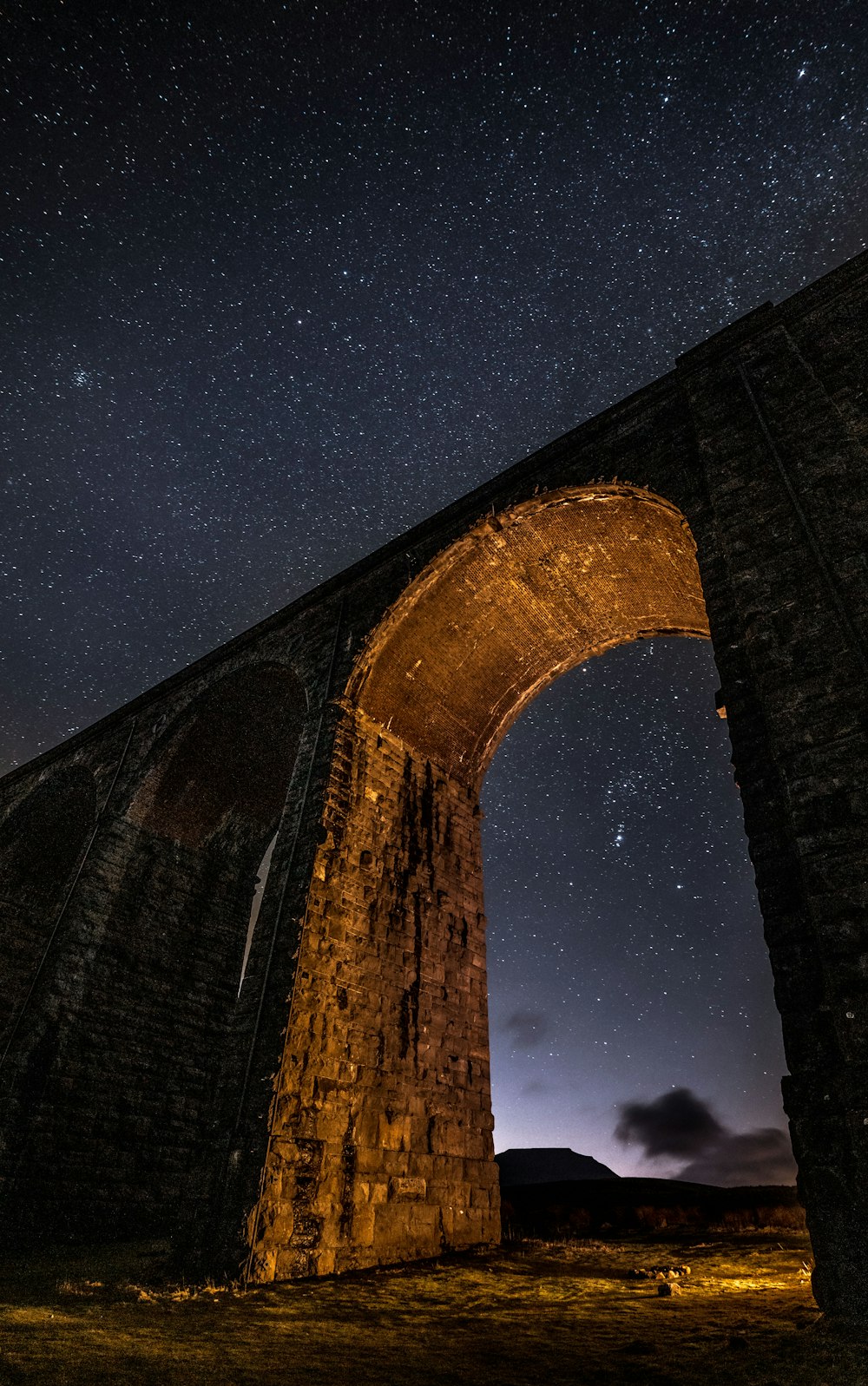 a stone bridge with a sky full of stars in the background