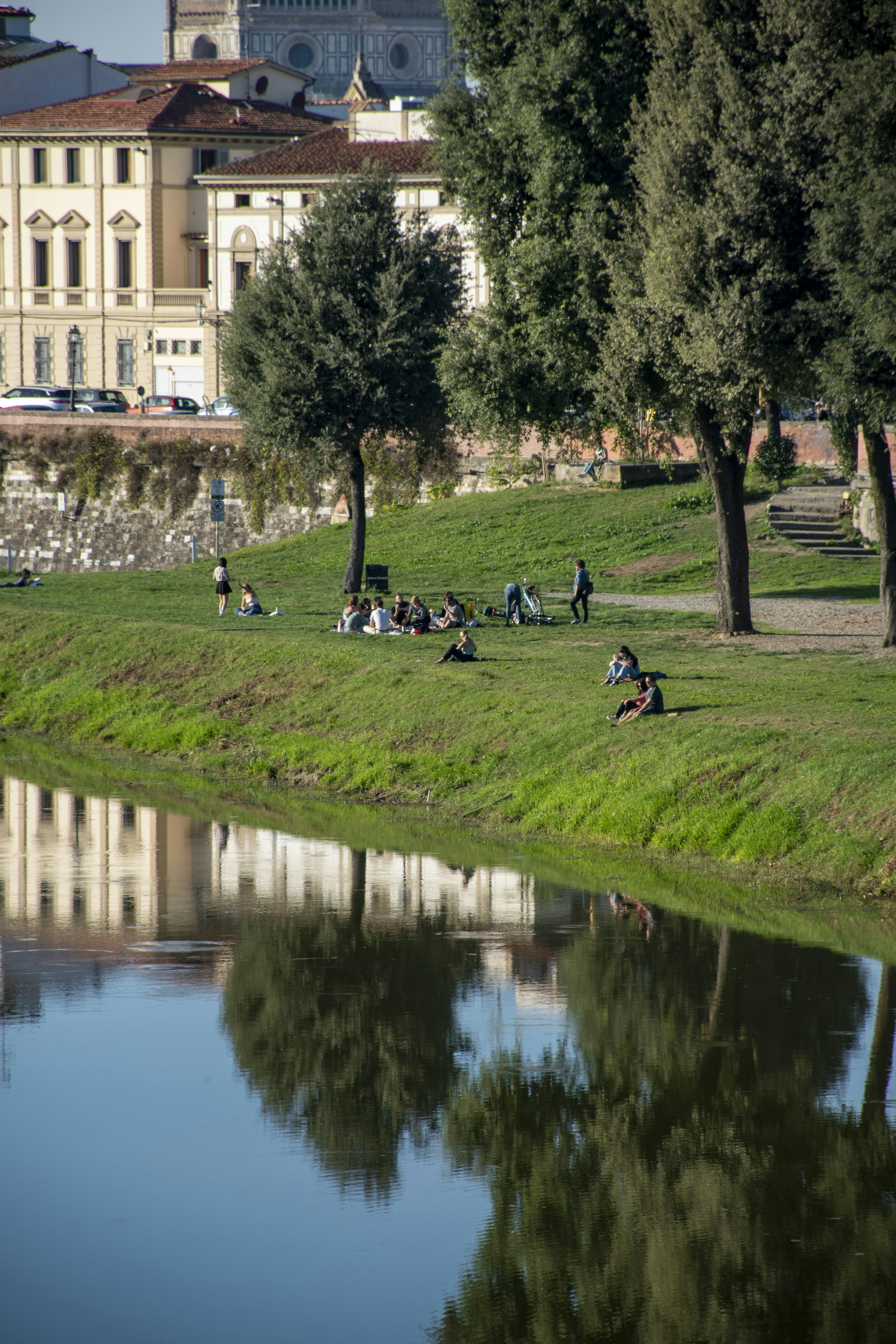 a group of people sitting on top of a lush green field next to a river