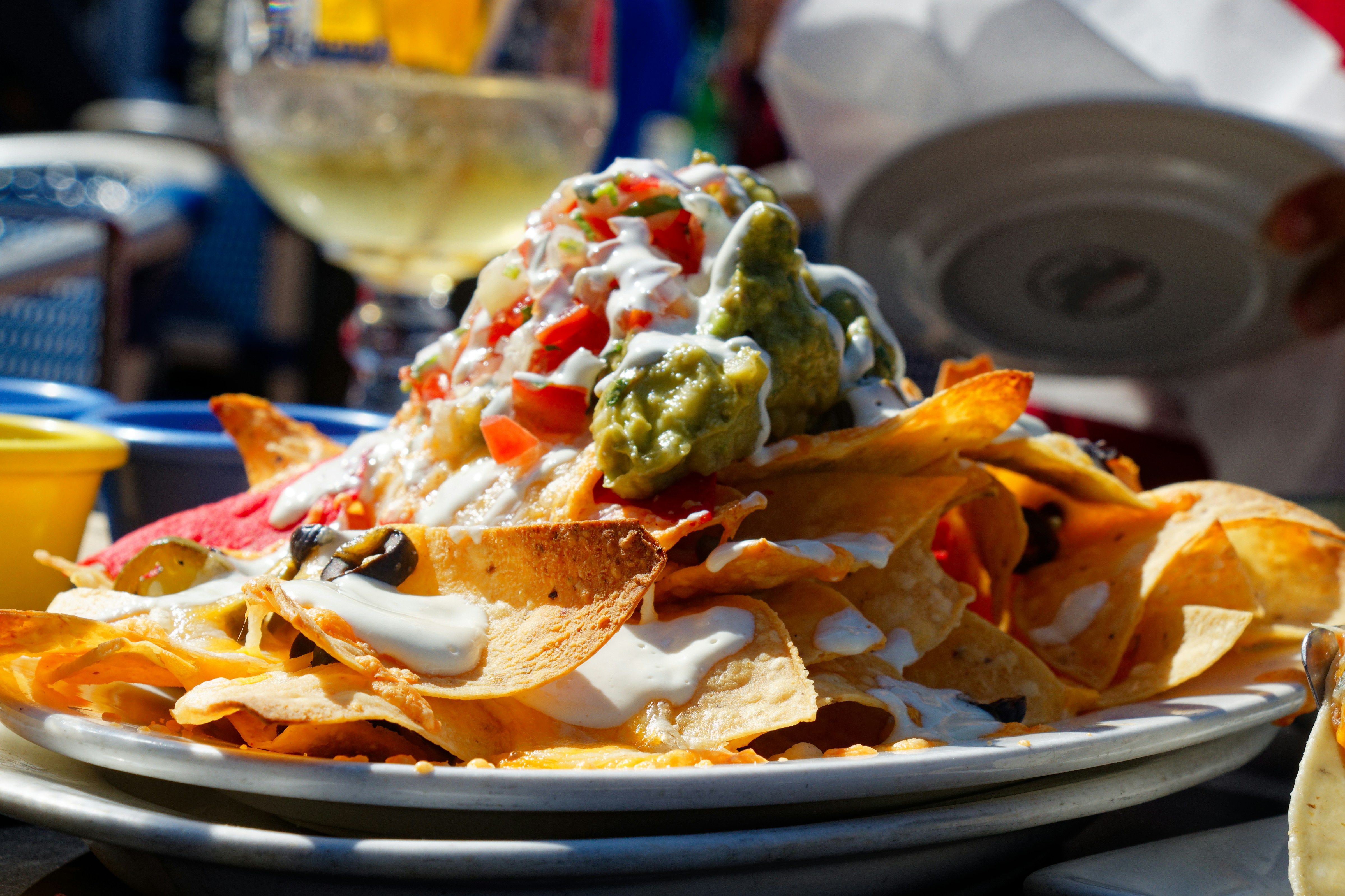 Towering loaded nachos with golden queso, fresh jalapeños and colorful toppings on dark slate