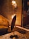 A warmly lit interior features a modern floor lamp with multiple cylindrical shades, casting a soft light against a textured wall. The room includes a plush armchair with rich fabric and a sleek wooden table with a marble top. The overall design aesthetics are sophisticated and cozy.