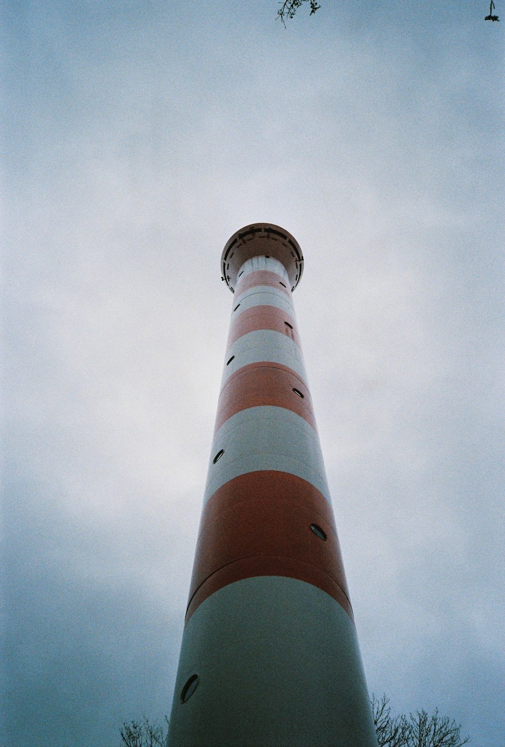 a tall red and white lighthouse under a cloudy sky