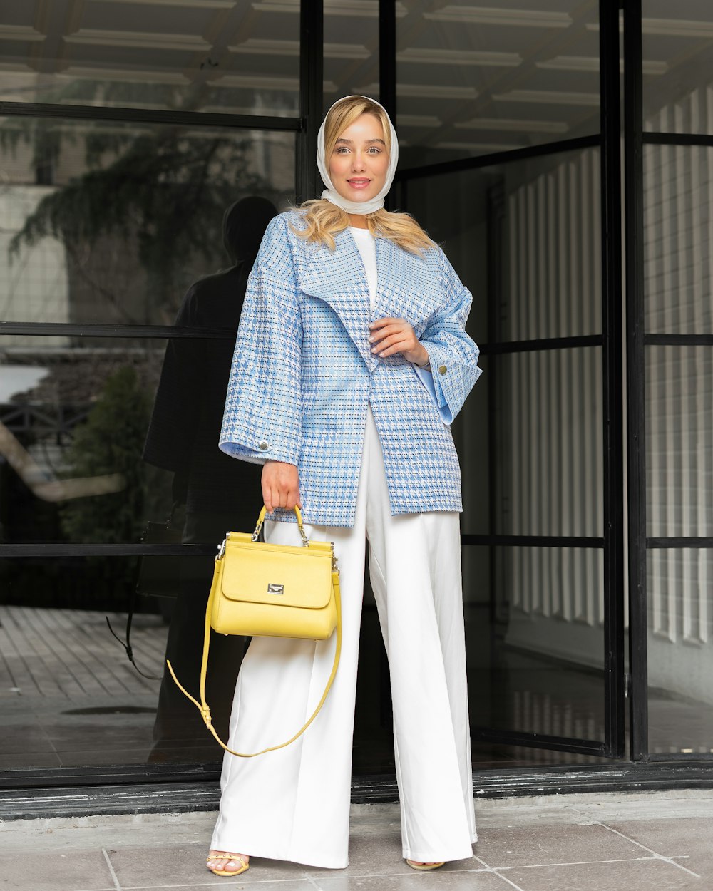 a woman in a blue coat and white pants holding a yellow purse