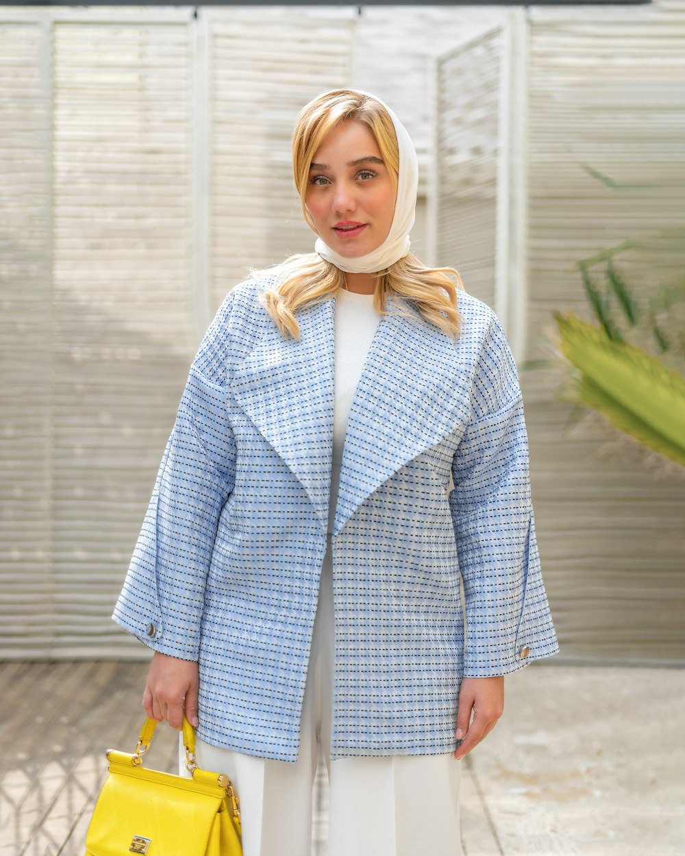 a woman in a blue jacket and white pants holding a yellow purse