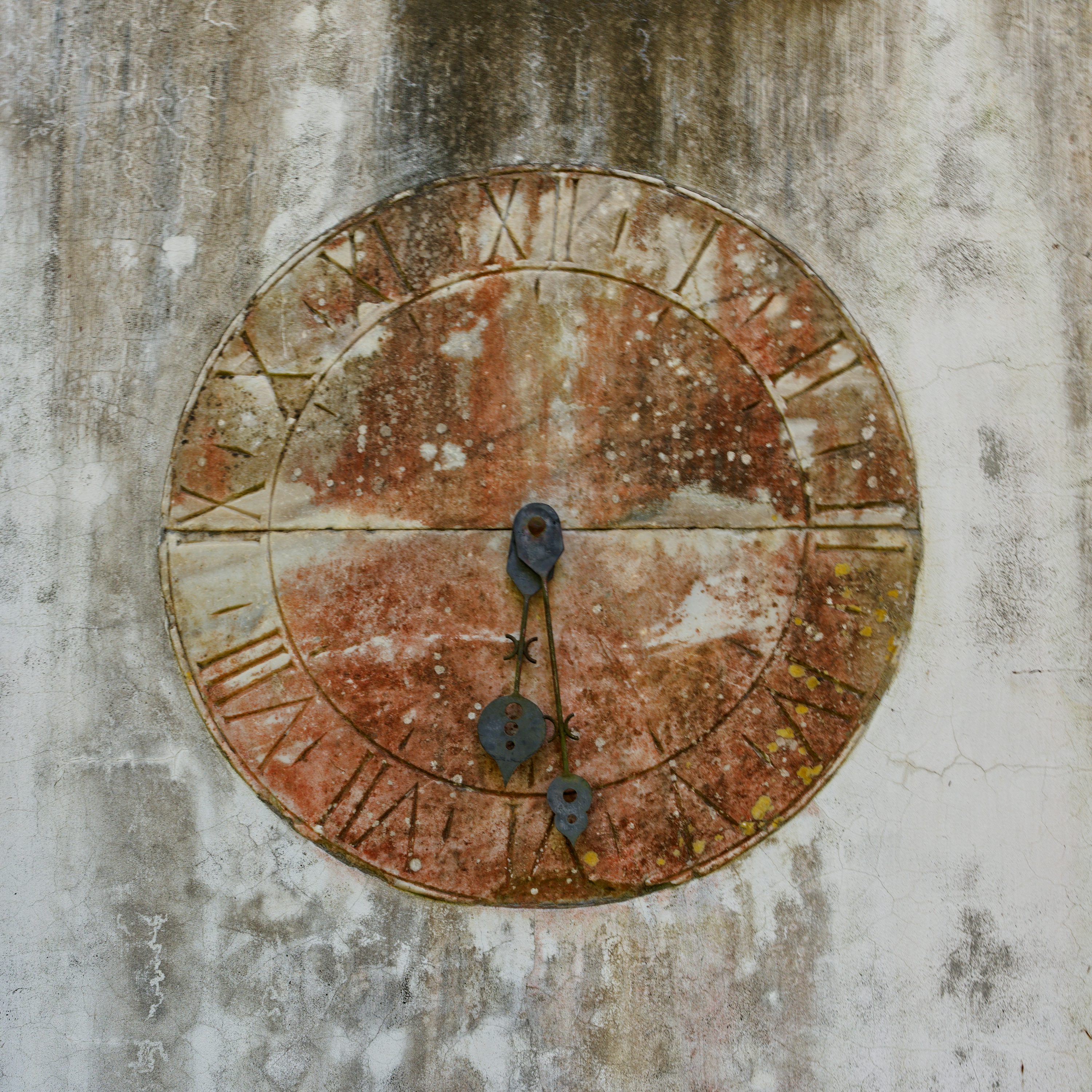 a rusty clock with roman numerals on a concrete wall