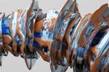 A complex, abstract form composed of swirling, intertwined materials with a glossy texture. The structure appears to be a fusion of metallic and clay-like elements, with smooth and flowing lines.