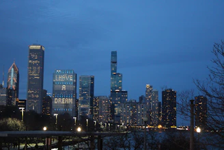Elegant nighttime city skyline with illuminated financial district buildings under a deep blue sky.