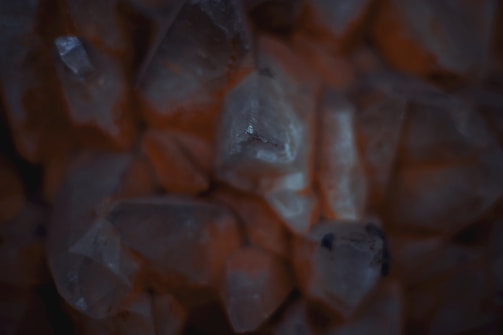 Clusters of translucent crystals with a dark and moody lighting. The crystals have a natural and rough texture, appearing orange and grayish in hue.