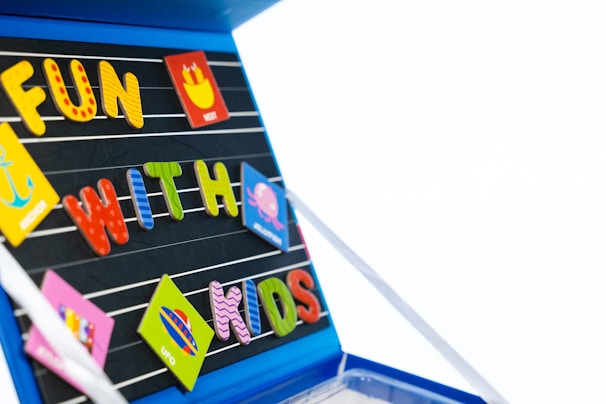 Brightly colored magnetic letters and shapes arranged on a black surface. Different colors and shapes give a playful and educational feel. Text reads 'FUN WITH KIDS' made up of various colorful letters and accompanied by several playful magnets depicting different objects.