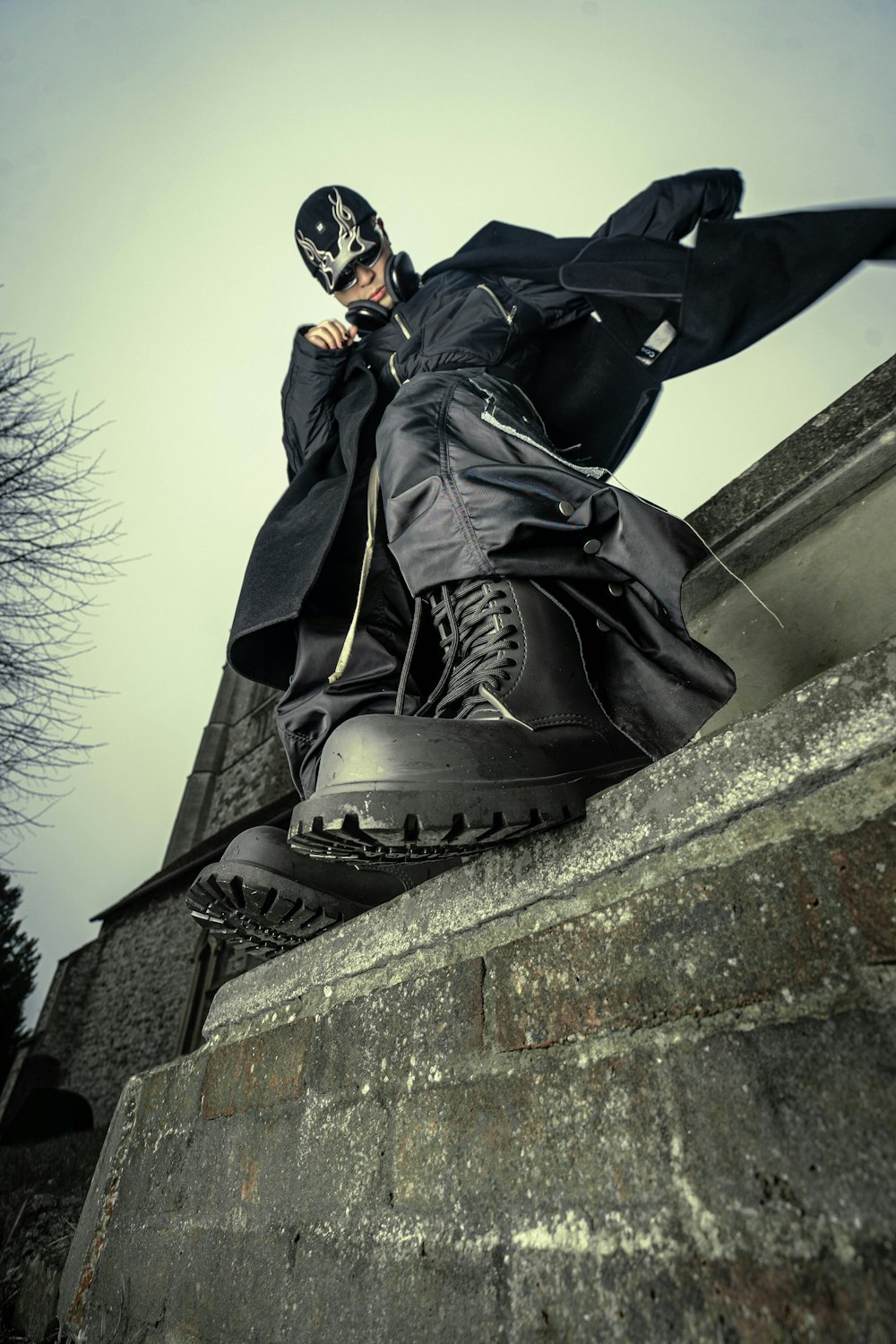 a man in a black coat and hat is sitting on a ledge