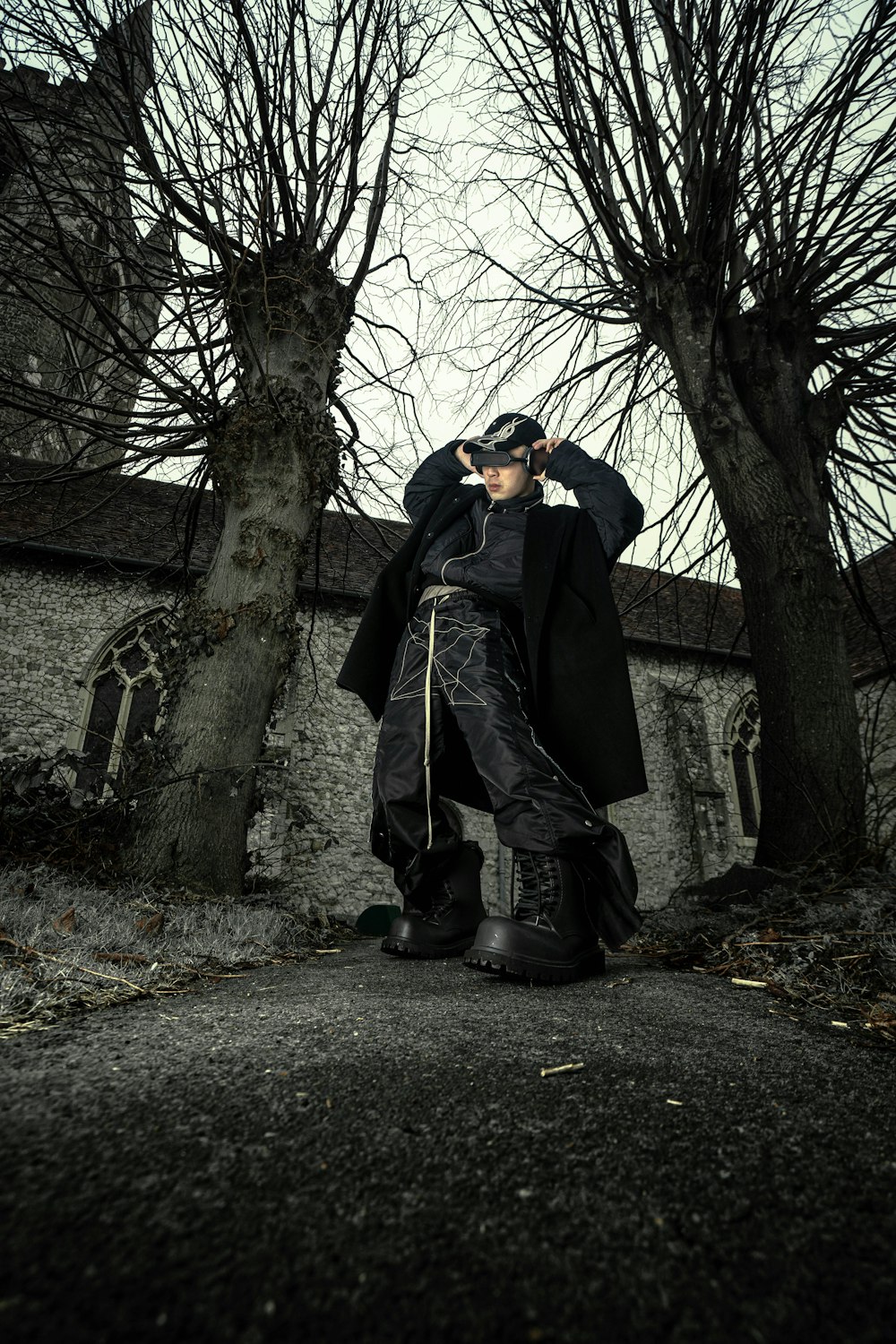 a man in a black coat and black pants standing in front of a tree